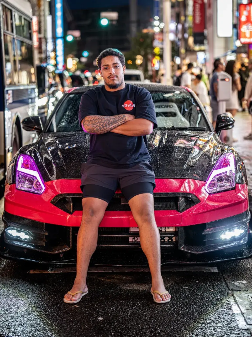 San, tu conductor y guía, sentado en el capó del GT-R rosa en Tokio de noche